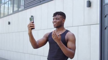 Afro-Amerikalı sporcu telefonda konuşuyor ve sokakta gülümsüyor, sporcu çocuk video ve trenlerle internetten iletişim kuruyor.