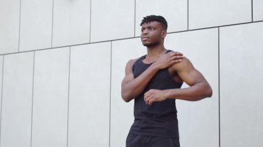 Spor giyimli Afrikalı Amerikalı bir adam sokakta ısınma egzersizleri yapıyor ve kulaklıkla egzersiz yapıyor.
