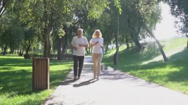 Yaşlı çift parkta koşuyor ve egzersiz yapıyor, gri saçlı emekliler spor yapıyor ve açık havada dinleniyor.