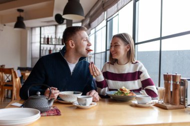 Genç çift kafede oturuyor ve öğle yemeği yiyorlar, erkek ve kız restoranda çay yiyip içiyorlar.