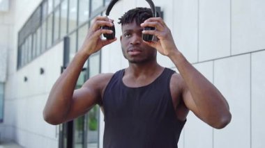 Atletik Afrikalı Amerikalı adam dışarıda kablosuz kulaklık takıyor, kaslı adam antrenmandan önce müzik dinliyor.