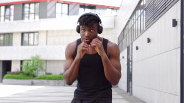 Spor giyimli Afro-Amerikan boksör, kulaklıklı, atletik adam, şehir arka planında boks yapıyor.