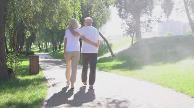 Birbirine aşık yaşlı bir çift parkta yürüyor ve el ele tutuşuyor, kır saçlı adam ve kadın ormanda yürüyor ve konuşuyor ve gülümsüyor,