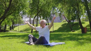 Sporcu yaşlı bir adam meditasyon yapar ve yazın parkta yoga yapar. Aktif gri saçlı emekli dışarıda nilüfer pozisyonunda oturur.