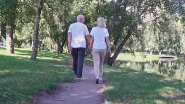 Birbirine aşık yaşlı bir çift parkta yürüyor ve el ele tutuşuyor, kır saçlı adam ve kadın ormanda yürüyor ve konuşuyor ve gülümsüyor,