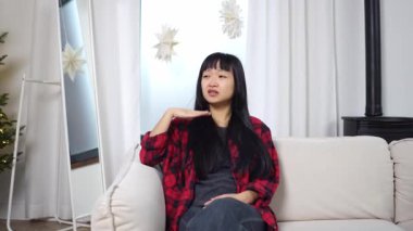 Kanepede sıcaktan muzdarip Asyalı genç bir kadın ve rüzgar için el sallayan sıcak hava ve iklimi gösteren bir kız.