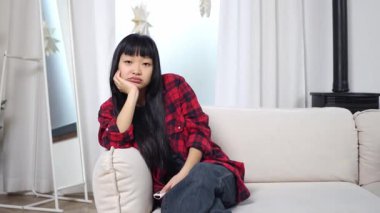Asyalı genç bir kadın televizyon seyrediyor ve sıkılmış, yorgun, üzgün bir kız kanepeye oturmuş, kanalı değiştiriyor ve tatminsizlik ve depresyon gösteriyor.