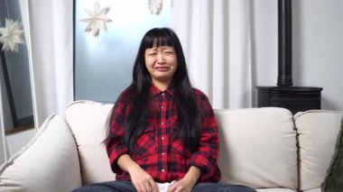 Genç Asyalı kadın hüzünlü bir film izler ve evde ağlar, mutsuz kız kanepede melodram izlerken gözyaşlarını ve endişelerini siler.