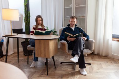 Genç çift sandalyede oturmuş masada kitap okuyor, kız ve erkek birlikte okuyor ve edebiyat okuyorlar.