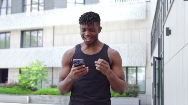 Afro-Amerikalı atlet akıllı telefon kullanıyor ve zaferini internette kutluyor, sporcu adam cep telefonunu tutuyor ve başarısından keyif alıyor.
