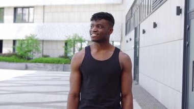 Spor giyim sektöründe Afro-Amerikalı bir adam şehir caddesinde kameraya bakıyor, atletik adam kollarını kavuşturup gülümsüyor.