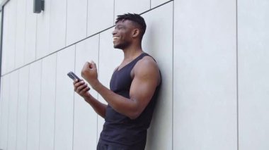 Afro-Amerikalı atlet akıllı telefon kullanıyor ve zaferini internette kutluyor, sporcu adam cep telefonunu tutuyor ve başarısından keyif alıyor.