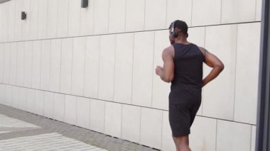 Genç Afro-Amerikalı adam dışarıda koşuyor ve kulaklıklı atletik adam şehir duvarına karşı spor yapıyor.