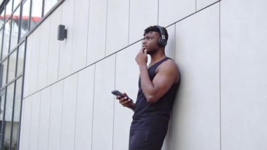 Akıllı telefon kullanan ve sokakta düşünen düşünceli Afro-Amerikan atletik adam. Mobil planlama ve hayal gücü olan kaslı adam.