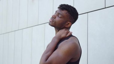 Afro-Amerikalı bir adam sokakta masaj yapar ve boynunu uzatır, atletik adam egzersiz yapmadan önce boyun kaslarını ısıtır ve acıdan muzdariptir.