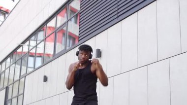 Spor giyimli Afro-Amerikan boksör, kulaklıklı, atletik adam, şehir arka planında boks yapıyor.