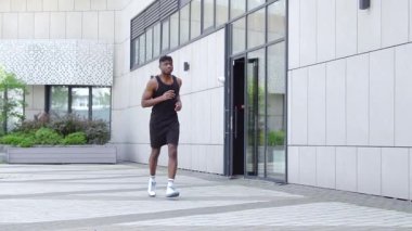 Genç Afro-Amerikalı adam dışarıda koşuyor ve kulaklıklı atletik adam şehir duvarına karşı spor yapıyor.