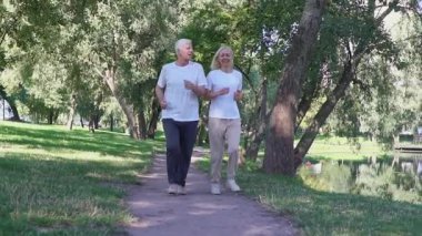 Yaşlı çift parkta koşuyor ve egzersiz yapıyor, gri saçlı emekliler spor yapıyor ve açık havada dinleniyor.