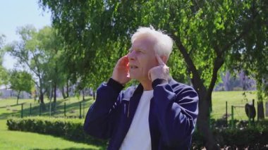 Yaşlı bir adam parkta baş ağrısından muzdarip, beyaz saçlı bir emekli şakağına masaj yapıyor ve dışarıda migren ağrısı gösteriyor.