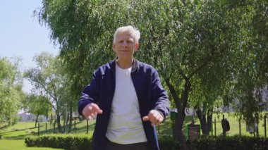 Mutlu yaşlı adam parktaki elleriyle kalbini gösteriyor. Gri saçlı emekli açık havada aşk ve romantizm jesti gösteriyor.