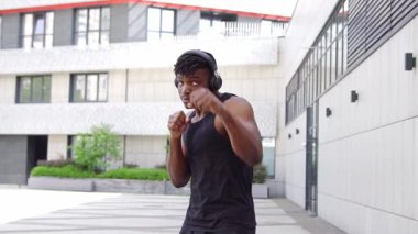 Spor giyimli Afro-Amerikan boksör, kulaklıklı, atletik adam, şehir arka planında boks yapıyor.