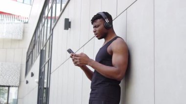 Şaşırmış Afrikalı Amerikalı atletik adam akıllı telefon kullanıyor ve sokakta facepalm gösteriyor, cep telefonu olan kaslı adam internette kaybediyor ve hatalar yapıyor.