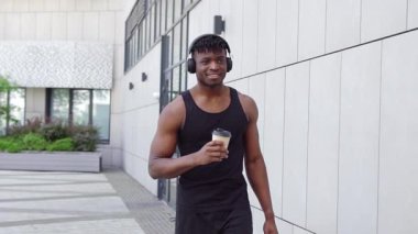 Spor kıyafetli Afro-Amerikalı bir adam kahve içiyor, müzik dinliyor, ve şehir sokaklarında yürüyor, kulaklıklı bir adam şehir arka planına karşı yürüyor.