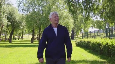 Yaşlı yaşlılar yazın parkta yürürler ve gülümserler, mutlu gri saçlı emekliler doğada yalnız yürürler.