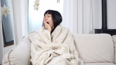 Battaniyeyle kaplanmış Asyalı genç bir kadın uykusuzluk çekiyor, uykulu bir kız televizyon izlemekten yoruldu ve sıkıldı.