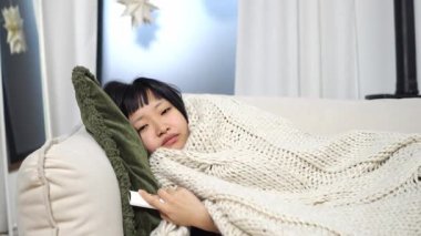 Asyalı yorgun kız kanepede uzanmış televizyon seyrediyor ve evde uyuyakalıyor. Uykulu kadın uzaktan kumandayla gözlerini kapatıyor.