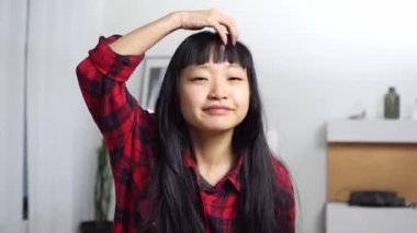 Asyalı mutlu kız hazırlanıyor ve aynaya bakıyor. Saçını düzeltiyor ve görünüşüne özen gösteriyor. Kendine gülümseyen mutlu kadın.