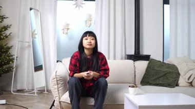 Genç Asyalı bir kadın televizyon seyrediyor ve korkuyor ve elleriyle yüzünü örtüyor. Kanepede oturan şok olmuş bir kız korku filmi izliyor.