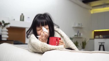 Battaniyeyle kaplanmış hasta, genç Asyalı bir kadın evde soğuk ve akan bir burundan muzdarip. Mutsuz kız burnunu mendillerle siliyor ve grip belirtileri gösteriyor.