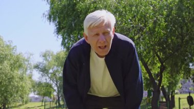 Yorgun yaşlı adam parkta egzersiz yapıyor ve soluklanmaya başlıyor. Yorgun, kır saçlı emekli, dışarıda koştuktan sonra sıcaktan muzdarip.