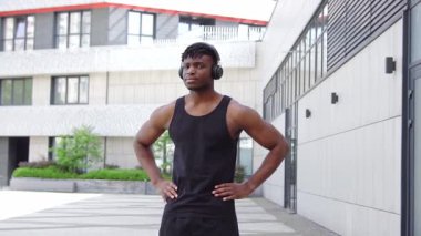 Spor giyim sektöründe Afro-Amerikalı bir adam şehir caddesinde kameraya bakıyor, atletik adam kollarını kavuşturup gülümsüyor.