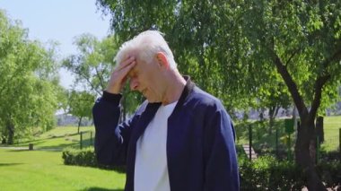 Yaşlı bir adam parkta baş ağrısından muzdarip, beyaz saçlı bir emekli şakağına masaj yapıyor ve dışarıda migren ağrısı gösteriyor.