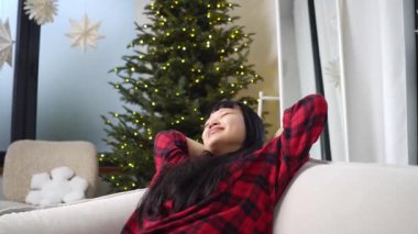 Genç Asyalı kadın rahat bir kanepede uzanıyor ve rüya görüyor. Kız kanepede uzanıyor düşünüyor ve gülümsüyor.