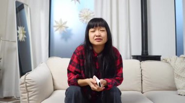 Asyalı kızgın kız TV izliyor ve hayal kırıklığı ve hayal kırıklığı içinde çığlık atıyor, üzgün kadın TV 'ye konuşuyor ve küfür ediyor.