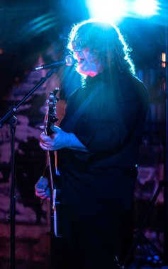 Man singing and playing bass on stage with backlit blue and pink lights - live music event concept