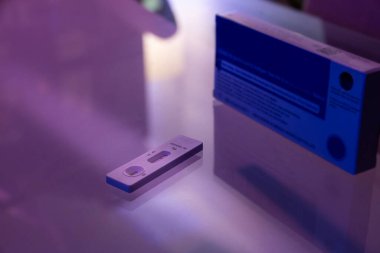 Yansıtıcı yüzeyde negatif sonuç veren bir COVID testi. Test paketlemesi arka planda görülebilir. Sahne ciddi ve odaklı.