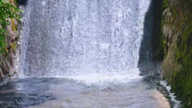 Şelalenin ayrıntıları. Su aşağı akar ve yoğun bir su perdesi oluşturur. Su berrak ve sakin. Huzurlu bir atmosfer yaratıyor. Görüntü doğanın güzelliğini ve gücünü yakalar.