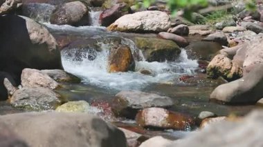 Kayaların üzerinden akan suya yakın bir dağ deresinde küçük akıntılar ve beyaz köpükler yaratıyor.