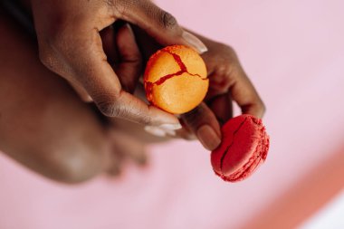 Afro-Amerikan bir kadının ellerinde pembe arka planda makarna kurabiyeleri.