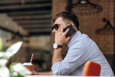Yakışıklı esmer adam kafede yan oturup telefonda konuşuyor.