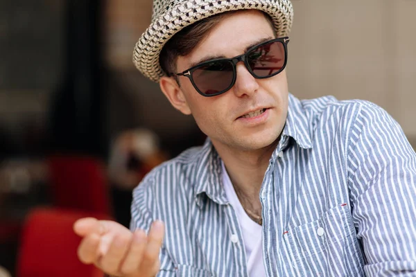 Handsome Man Hat Sunglasses Sits Cafe Points Something His Hand — Stock Photo, Image