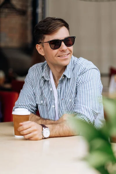 炎热的夏天 一个戴着太阳镜的英俊的黑发男人在咖啡店里喝杯咖啡时微笑着 — 图库照片