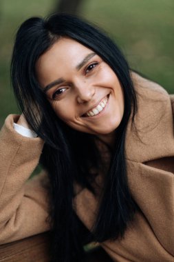 Kahverengi ceketli güzel esmer kameraya bakarken gülümsüyor. Portre