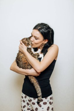 Genç, güzel esmer, kollarında bir kediyi öpüyor.