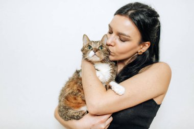 Genç, güzel esmer, kollarında bir kediyi öpüyor.