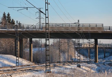 Demiryolu rayları ve yüksek gerilim hattı bir kış günü beton bir köprüden geçiyor.